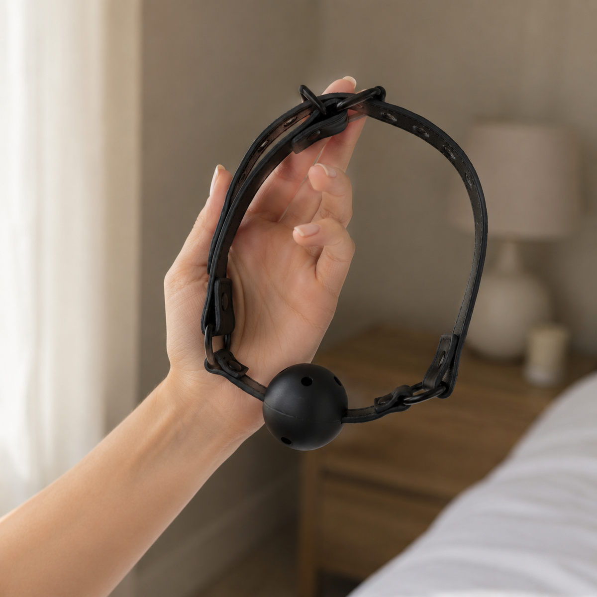 Hand houdt een zwarte ball gag met geventileerde siliconen bal en verstelbare band vast