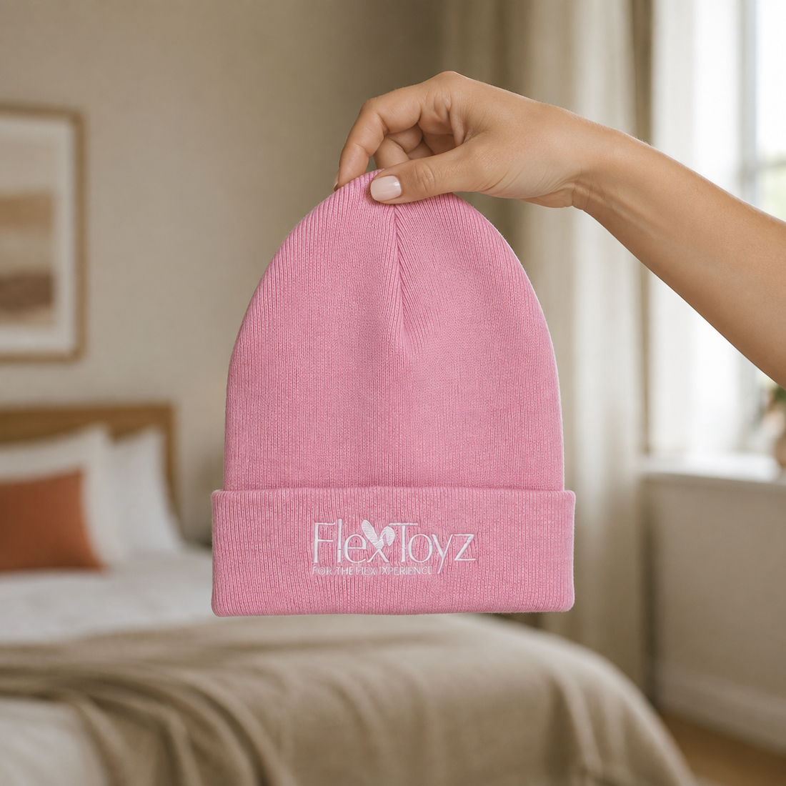 Hand houdt roze FlexToyz beanie met wit borduurlogo voor schaalweergave