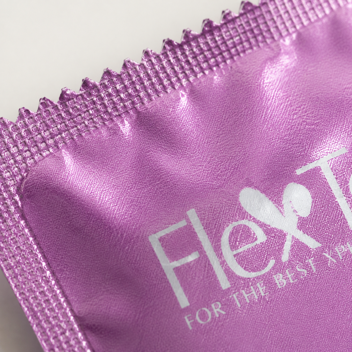 Macrodetail van roze folietextuur en gesealde rand van FlexToyz condoomverpakking