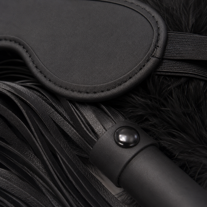 Detailfoto van het zwarte oogmasker, de kunstleren flogger en zachte veren van BondageKit 2