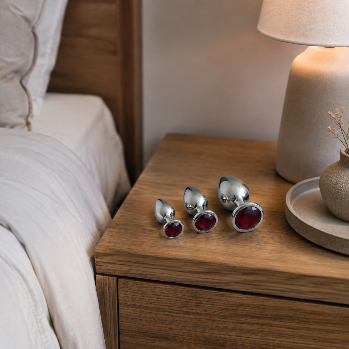 Zilveren buttplug set met rode diamant op een houten nachtkastje in een warme slaapkamer