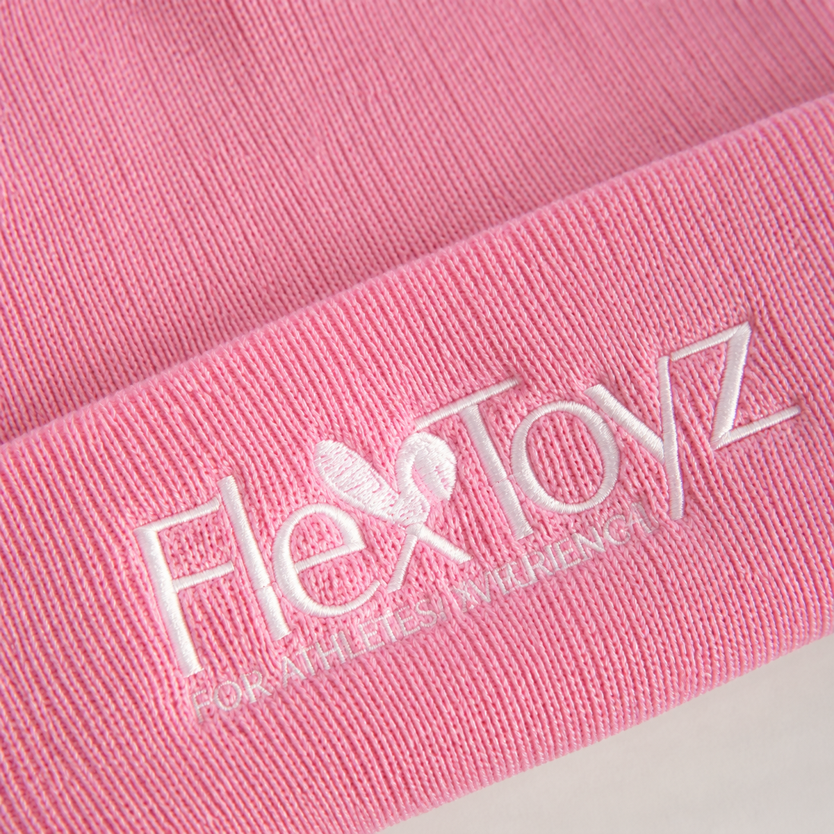 Macrodetail van roze ribbreisel en wit geborduurd FlexToyz logo op de beanie