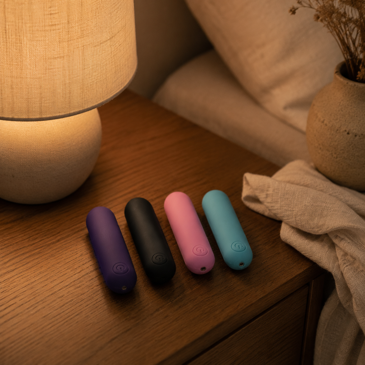 Vier FlexToyz bullet vibrators op warm houten nachtkastje naast zachte lamp
