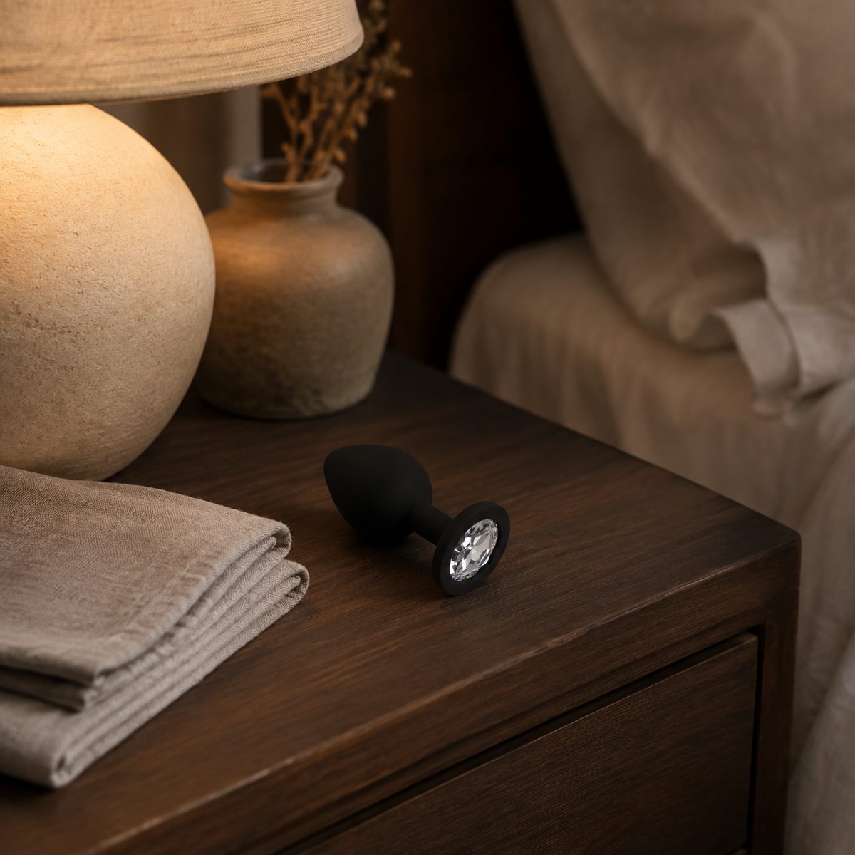 Zwarte FlexToyz buttplug Medium met witte diamant op warm houten nachtkastje