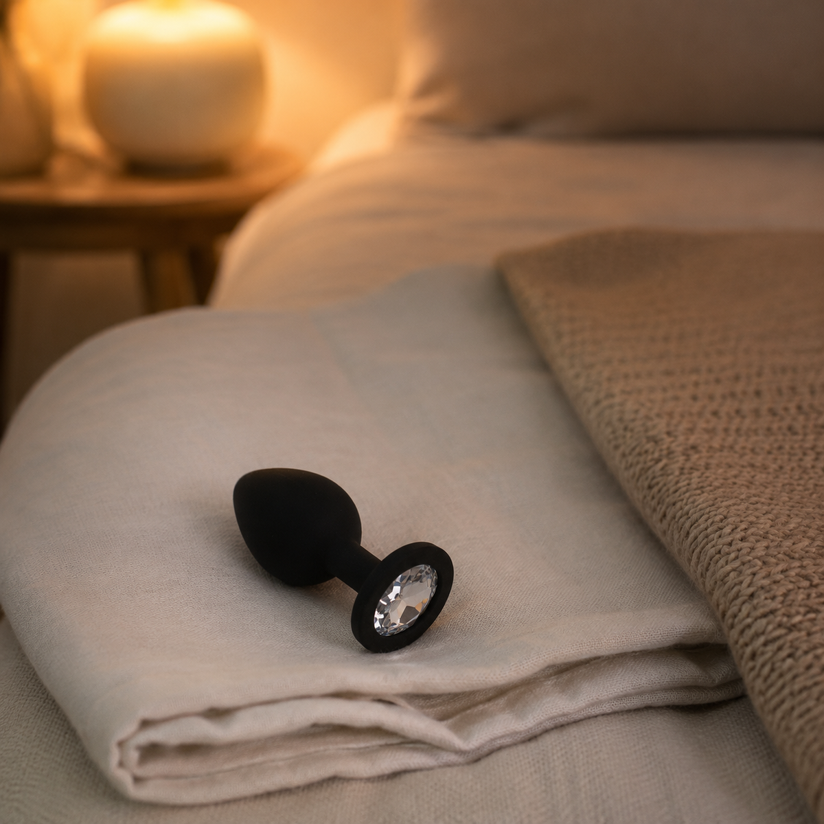 Zwarte FlexToyz buttplug Small met witte diamant op gevouwen linnen in warme slaapkamer