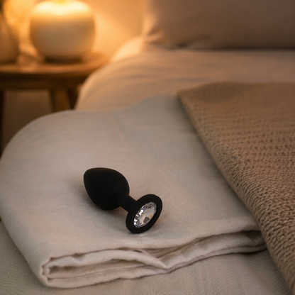 Zwarte FlexToyz buttplug Small met witte diamant op gevouwen linnen in warme slaapkamer